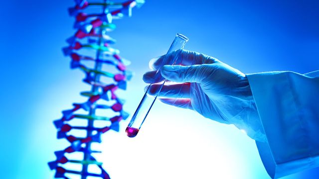 Someone holding a test tube in front of a model of DNA. 