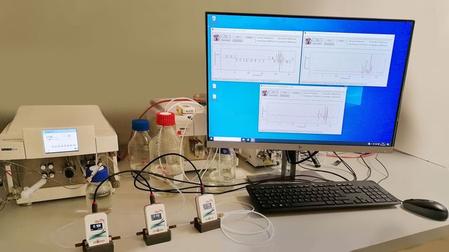 A computer screen next to 3 HPLC machines. 