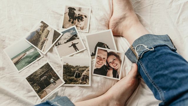 A person sits on a white sheet, with photos next to them. 