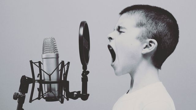 A young boy sings into a microphone. 