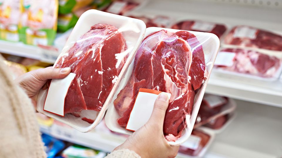 Hands hold two packaged joints of meat in a grocery store.