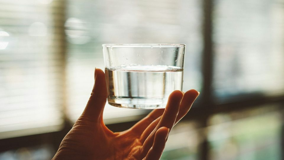 A person holds a small glass of water aloft with their fingertips.