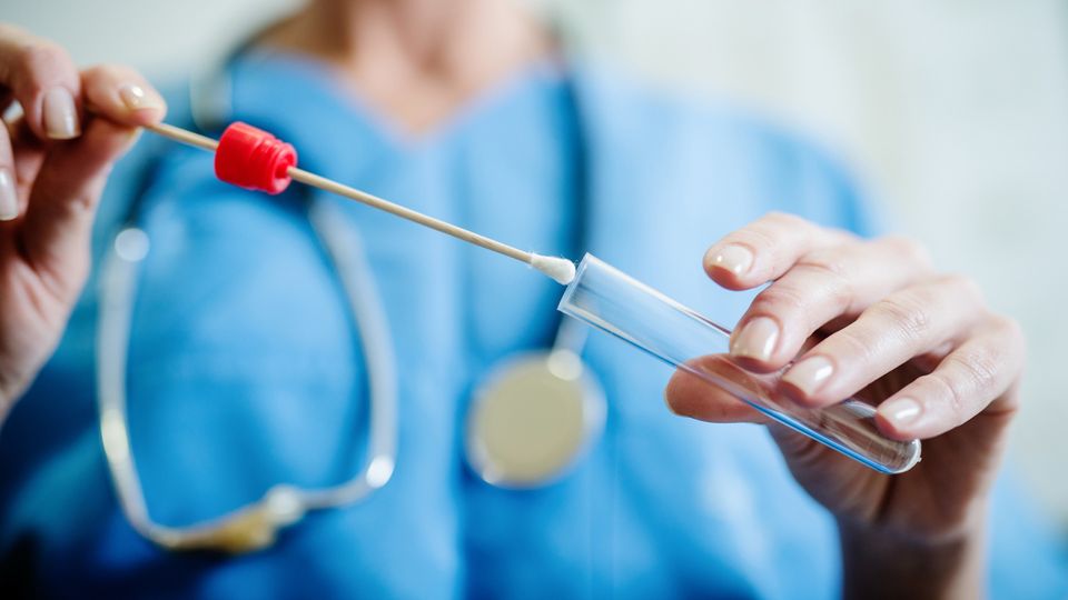 A doctor holds an empty saliva sample tube.